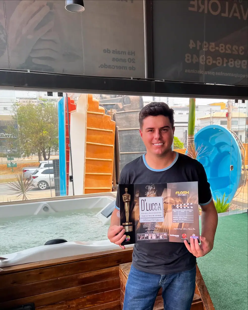 Representante da D'Lucca Piscinas com o certificado do prêmio VIP'S 2024 em mãos, na loja, ao lado de um spa em exposição